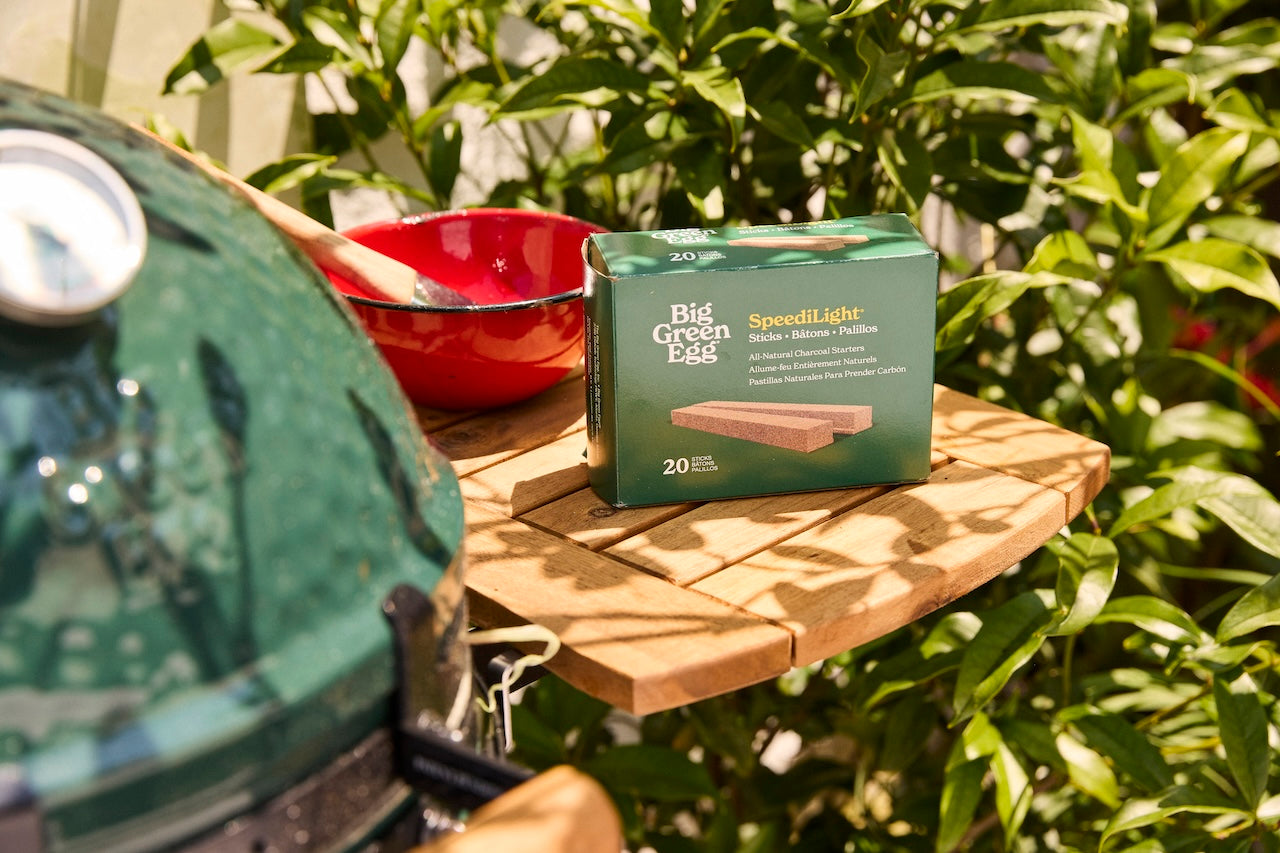 Big Green Egg grill with a box of Speedlight bulbs on a wooden surface outdoors.